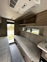 Bright RV rental interior with light wood cabinetry, a large sofa seating area, and a white AC unit on the ceiling.