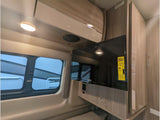 RV rental interior featuring a mounted flat-screen TV, modern overhead cabinets, and a window with blinds.