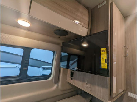 RV rental interior featuring a mounted flat-screen TV, modern overhead cabinets, and a window with blinds.