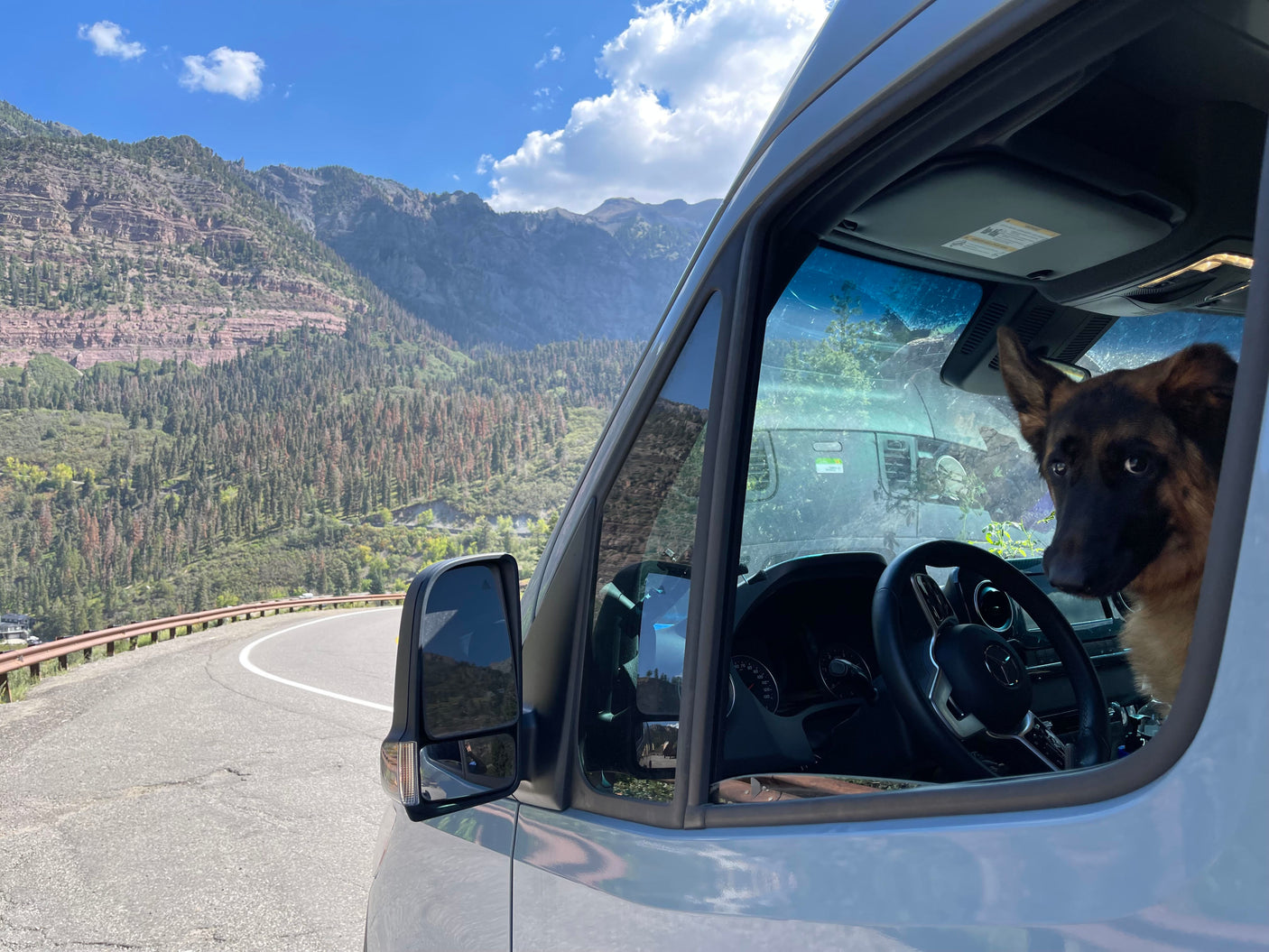 Scenic mountain road trip in an RV rental van with a German Shepherd looking out the window.