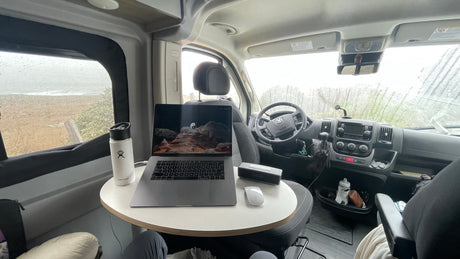 Cozy rv rental mobile office: laptop, Hydro Flask, and a rainy coastal view. Ideal for remote work & van life adventures.