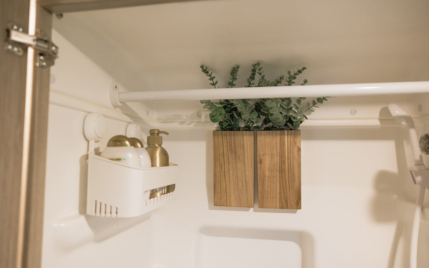 Compact RV rental shower: a white caddy with gold bottles, a decorative plant in wood holder, and shower fixtures.