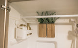 Compact RV rental shower: a white caddy with gold bottles, a decorative plant in wood holder, and shower fixtures.