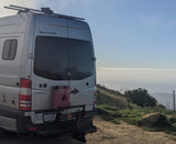 Rear view of a silver Sportsmobile Sprinter RV, equipped for adventure, at a scenic overlook above clouds. Great for an rv rental!