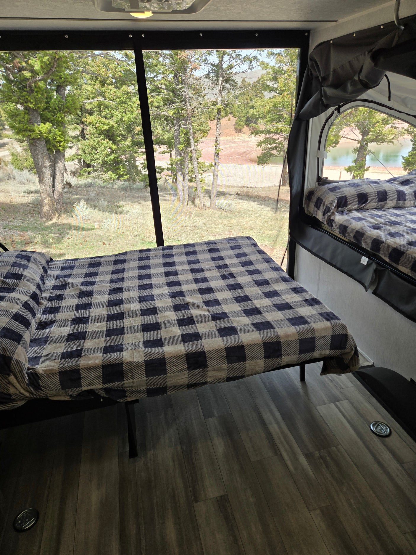Inside our RV rental, two comfy beds with checkered blankets offer a stunning nature view through large mesh windows, ideal for relaxing.