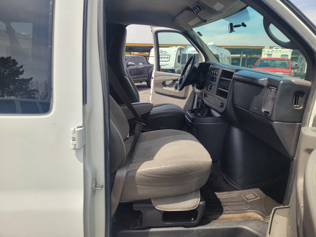 Interior of a white RV rental van, showing driver's seat and dash. Outside, various RVs and vehicles are visible in a parking lot.