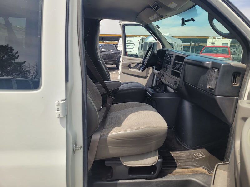 Interior of a white RV rental van, showing driver's seat and dash. Outside, various RVs and vehicles are visible in a parking lot. — photo 10
