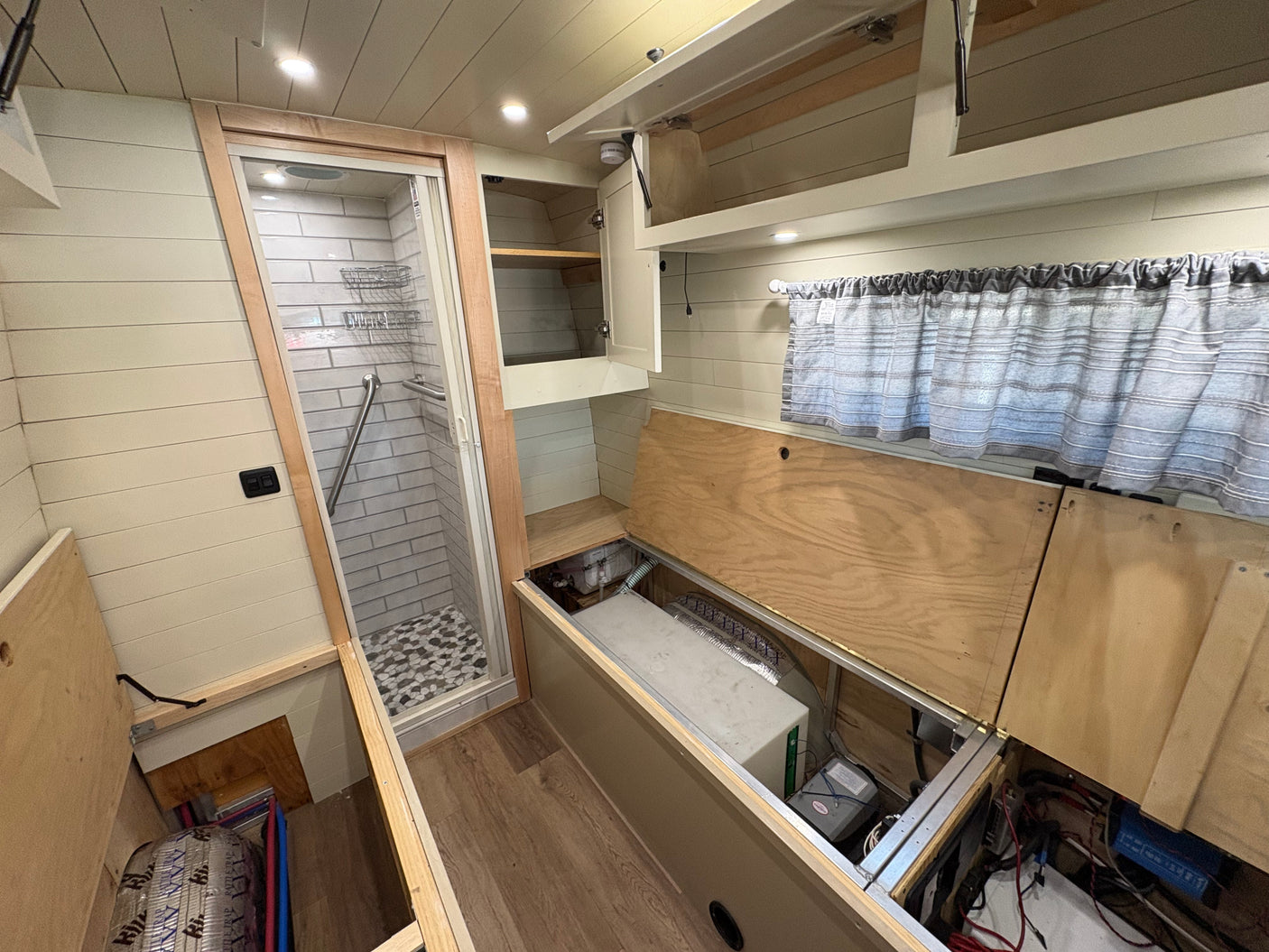 Inside this rv rental: a custom-built interior with a tiled shower, overhead storage, and accessible utilities for van life adventures.