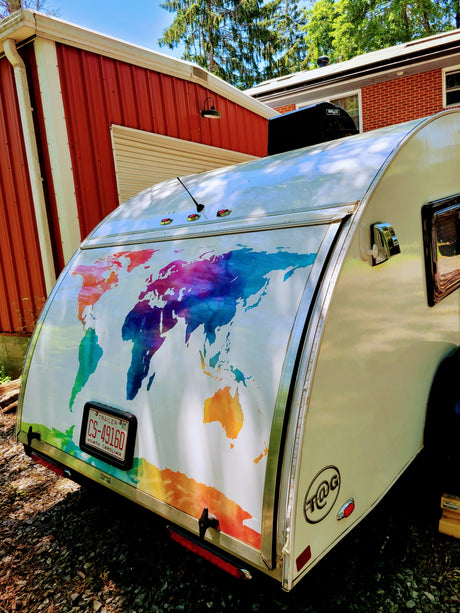 Experience adventure with this T@G teardrop **RV rental**! Features a vibrant world map on its rear, parked outside.