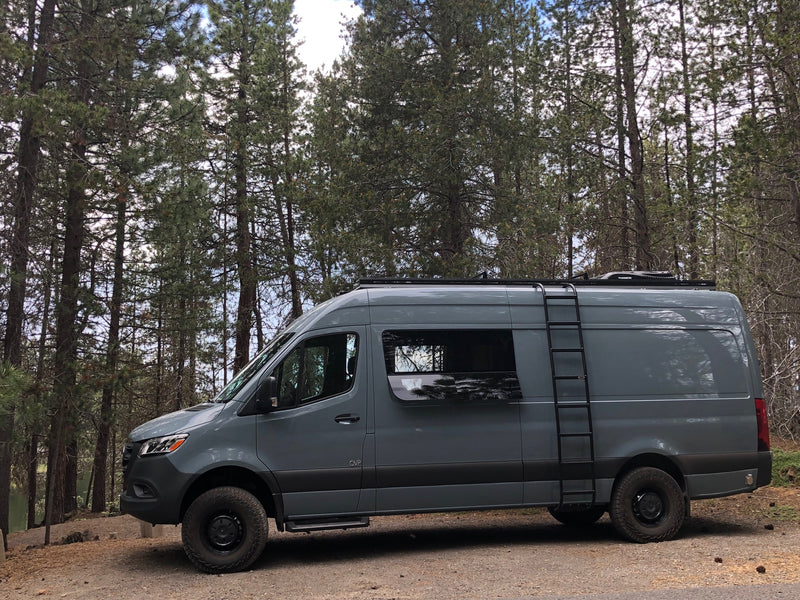 Gray Sprinter RV rental van with off-road tires and side ladder, parked in a scenic pine forest. — photo 3