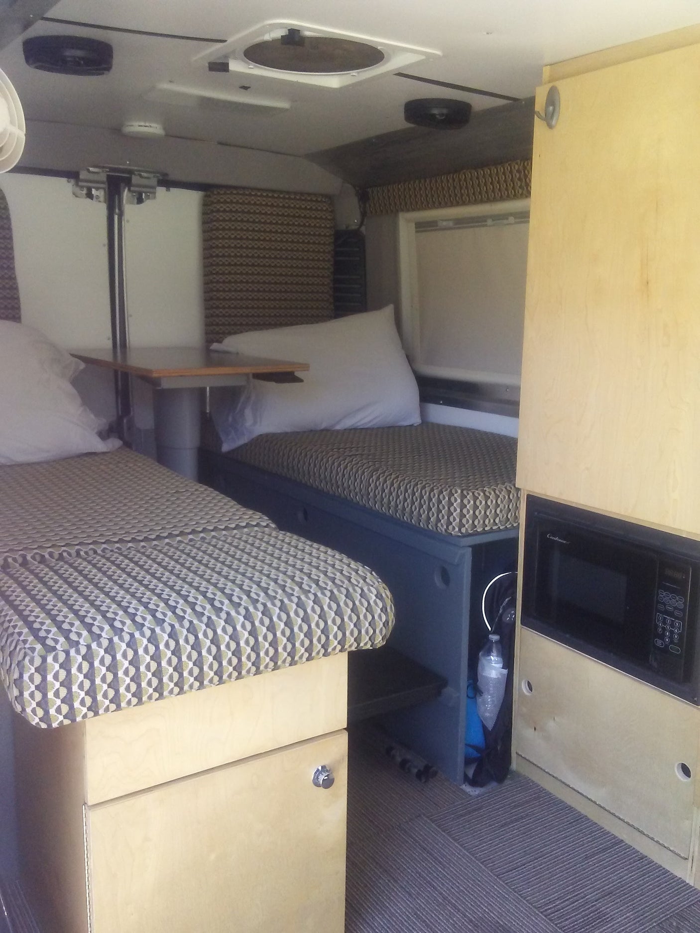 This RV rental interior features patterned benches, a versatile table, and overhead cabinets with a microwave.