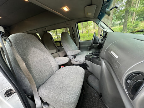 Inside an RV rental van: light grey fabric seats, detailed dashboard, and bright cabin lights, set for comfortable travel.