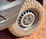 A dirty BFGoodrich off-road tire and Mercedes wheel on an RV rental, parked on a red dirt road.