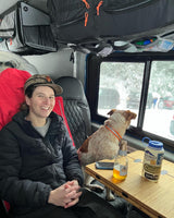 Inside a cozy rv rental, a person smiles while their dog looks out at a snowy winter scene. Perfect for van life adventures!