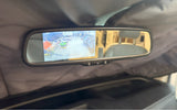Inside an RV rental, a rearview mirror displays a backup camera view of a garage with a van, ATV, and boat.