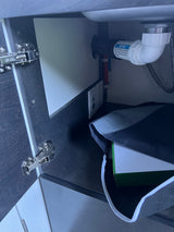 RV rental: Under-sink cabinet with plumbing, a waterless trap, red/blue water lines, and an electrical outlet with USB.