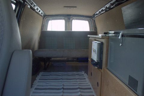 Inside a cozy RV rental: a modern camper van conversion featuring a bench seat, portable fridge, and heater for travel.