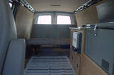 Inside a cozy RV rental: a modern camper van conversion featuring a bench seat, portable fridge, and heater for travel.
