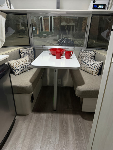 Cozy rv rental dinette with modern seating, a white table, red dishware, and patterned pillows. Perfect for travel adventures.