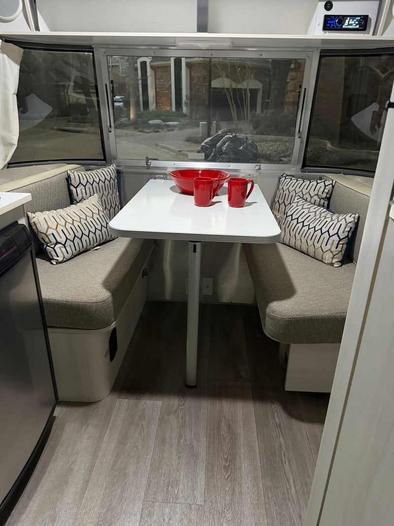 Cozy rv rental dinette with modern seating, a white table, red dishware, and patterned pillows. Perfect for travel adventures. — photo 4
