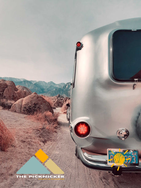 A shiny silver Airstream RV rental on a dirt road, amidst rugged desert rocks and distant mountains, ideal for adventure.