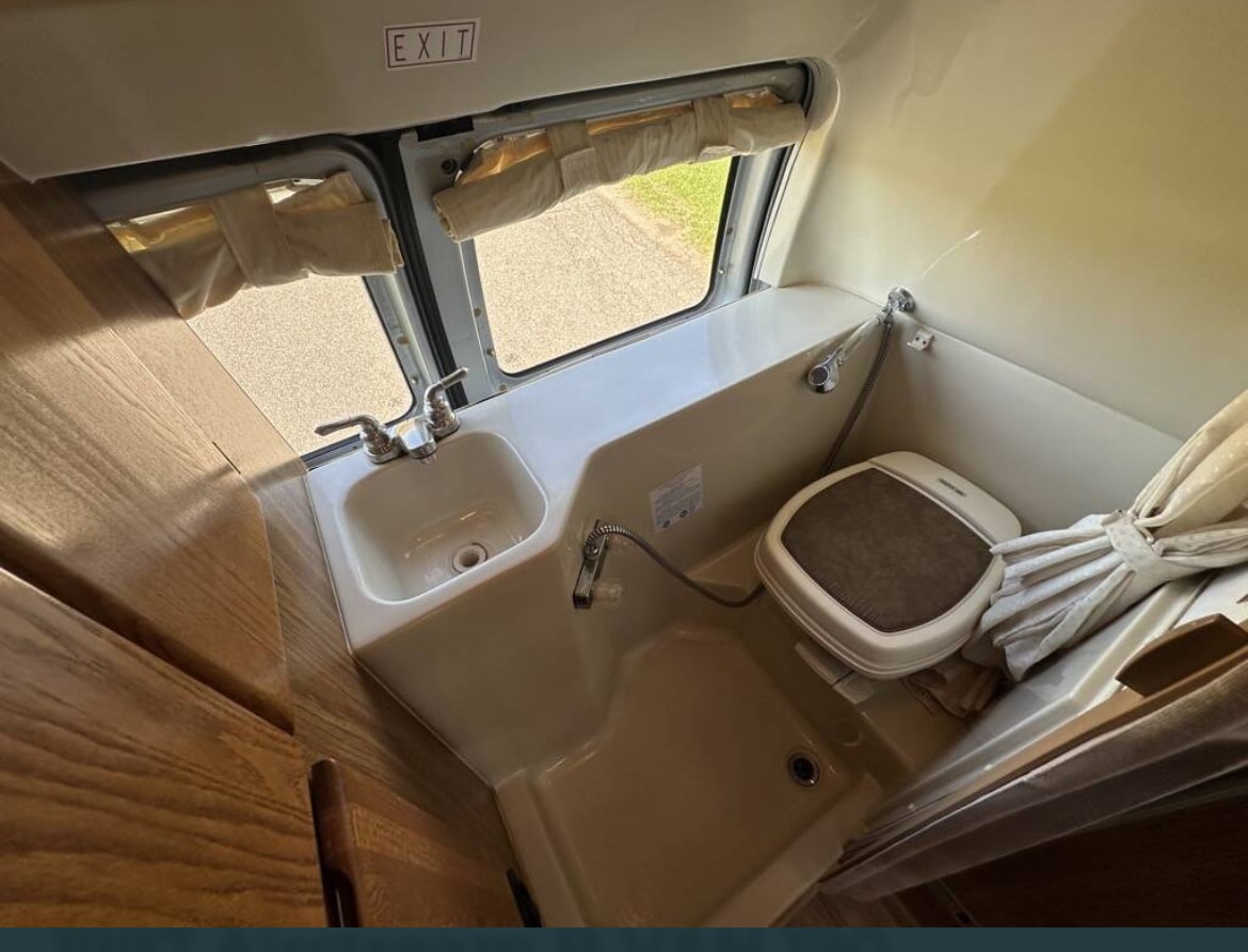 Compact RV rental wet bath featuring a sink, toilet, shower, and windows with "EXIT" sign above. — photo 17