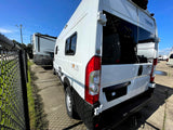 White Winnebago Solis camper van, ideal for your next RV rental adventure. Parked outdoors with fence shadows on concrete.