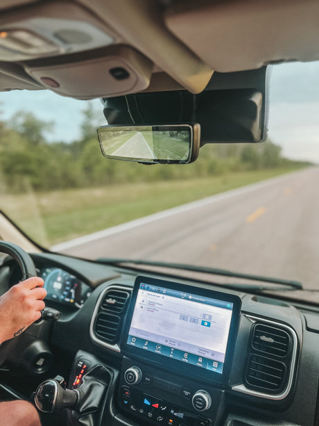 Inside an RV rental, driver's view with connected iPhones on the infotainment screen and a digital rearview mirror on "The Great Divide" route.