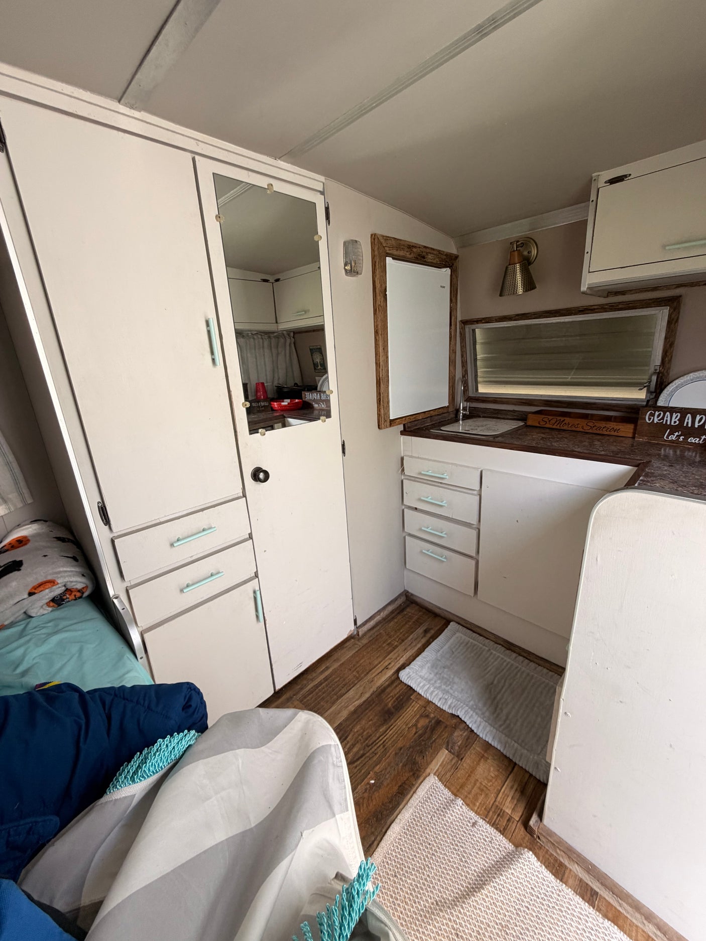 Cozy rv rental interior: white cabinets, wood floors, compact kitchen, and bed area. Ready for a road trip adventure.