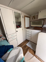 Cozy rv rental interior: white cabinets, wood floors, compact kitchen, and bed area. Ready for a road trip adventure.