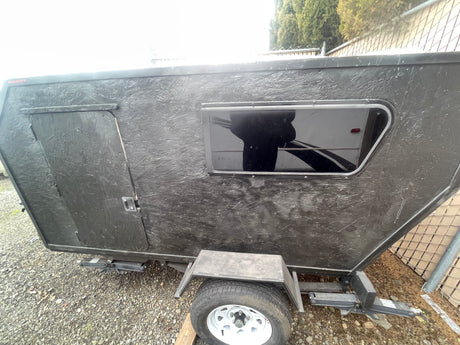 This compact black teardrop trailer, ideal for RV rental, features a side door, window, and textured exterior.
