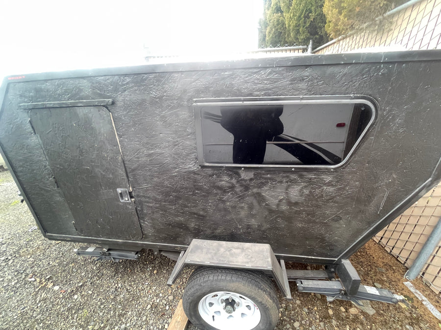 This compact black teardrop trailer, ideal for RV rental, features a side door, window, and textured exterior.