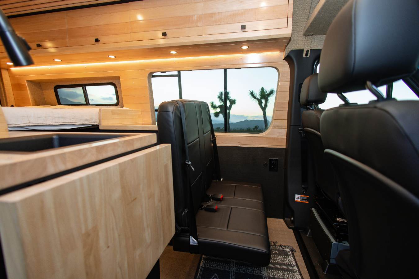 RV rental interior with custom wood cabinets, kitchen sink, bed, and passenger seats, showcasing a desert view.