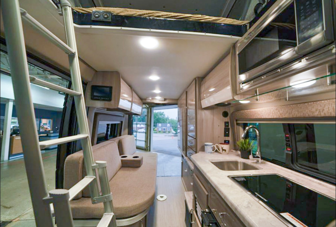 Modern rv rental interior showing a compact kitchen, sofa, and ladder to a loft bed, perfect for adventure travel.