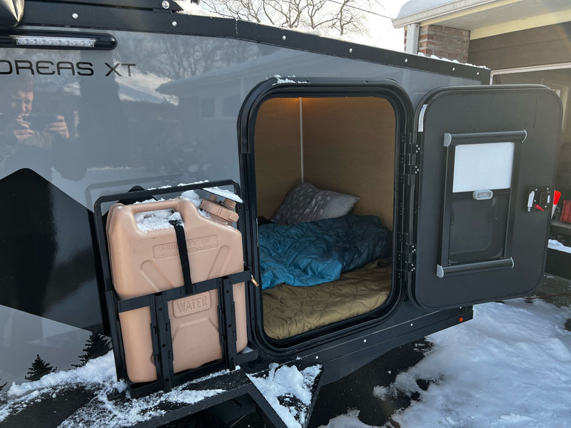  ready for winter adventure. Consider this RV rental for your travels!|Enjoy scenic outdoor adventure with an RV rental. Man washing dishes next to an off-road teardrop camper in mountains.|Compact rv rental with open side showing cozy bed and water storage — photo 5