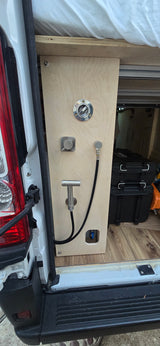 RV rental camper van's outdoor shower: wooden panel with water fill, mixer, spray nozzles, hose, and storage boxes.