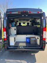 Experience van life in this RV rental! Rear view showing a customized interior with a convertible bed, storage, and kitchenette.