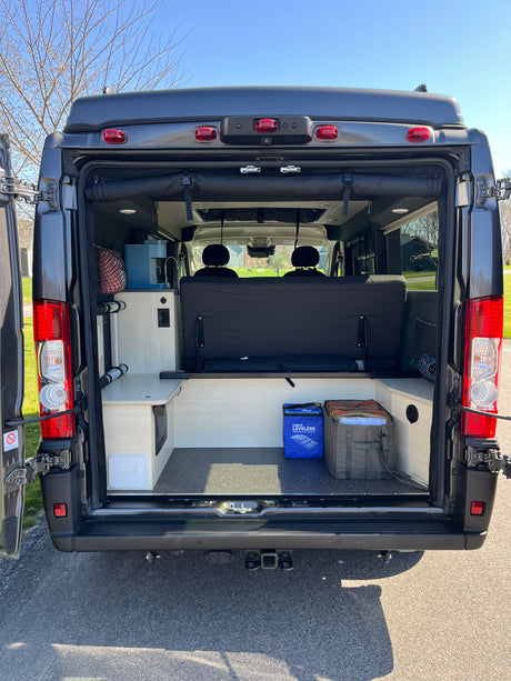 Experience van life in this RV rental! Rear view showing a customized interior with a convertible bed, storage, and kitchenette.