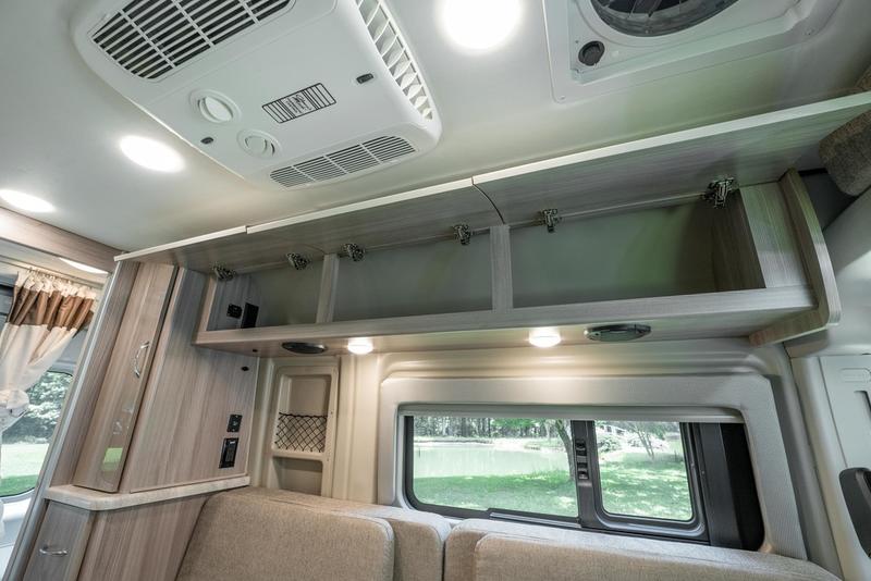 RV rental camper van interior showing open overhead storage, ceiling AC, cozy seating, and a window with outdoor views. — photo 17