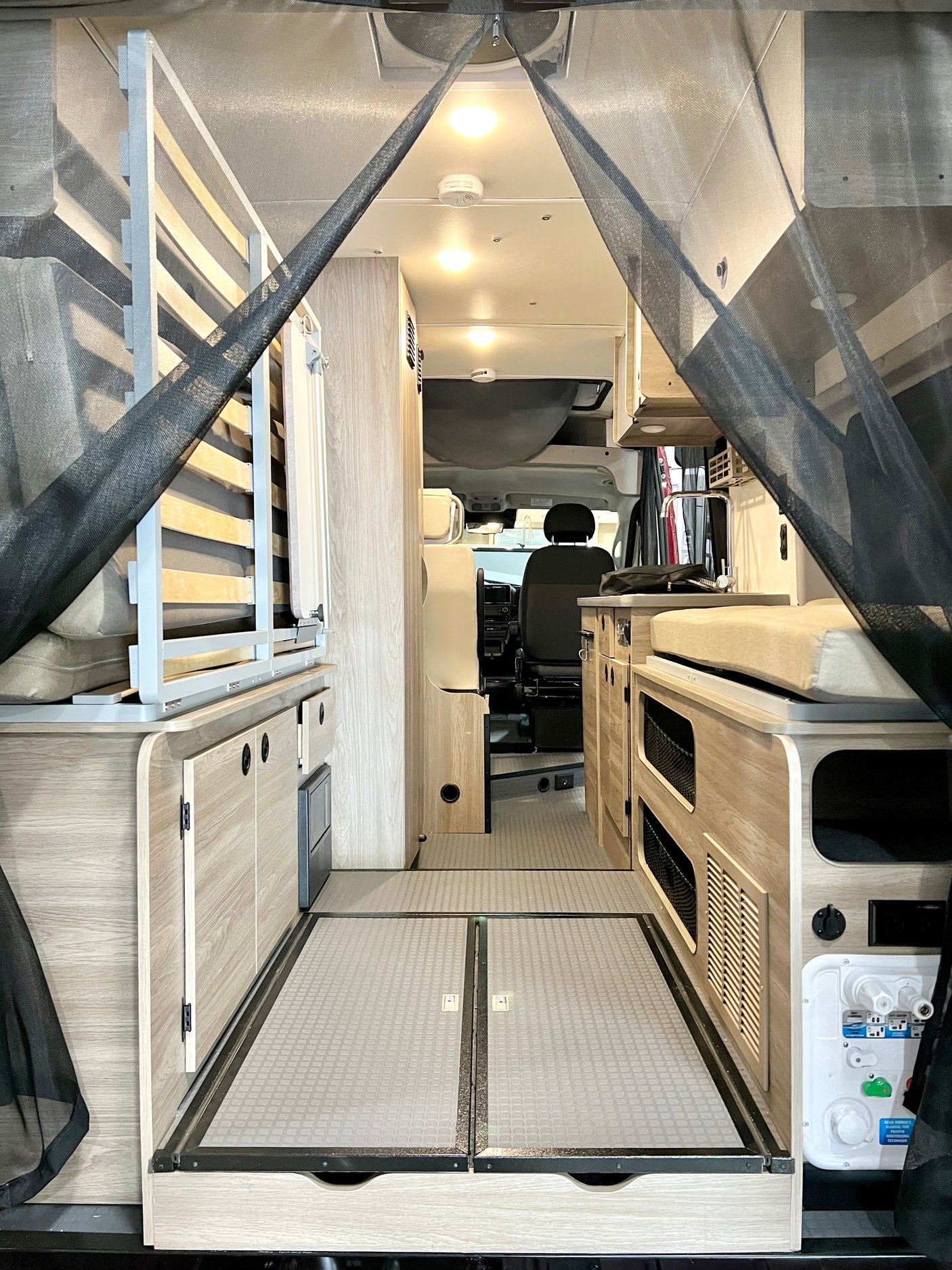 RV rental: Interior of a camper van with a bed/seating area, storage, and kitchen, viewed through a protective bug net.