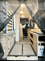 RV rental: Interior of a camper van with a bed/seating area, storage, and kitchen, viewed through a protective bug net.