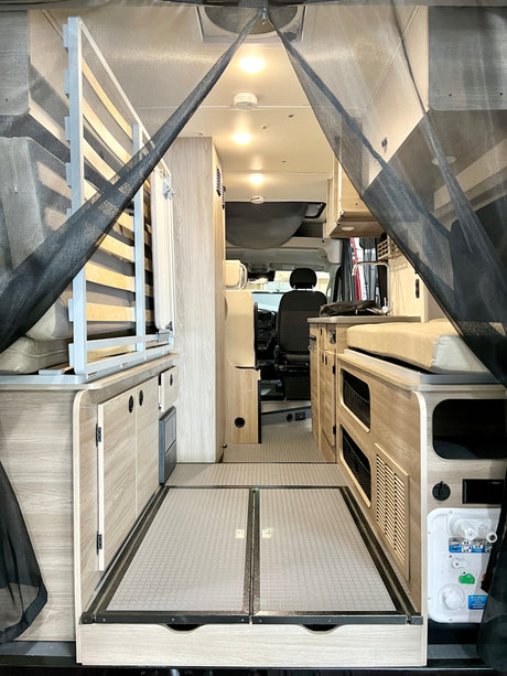 RV rental: Interior of a camper van with a bed/seating area, storage, and kitchen, viewed through a protective bug net.