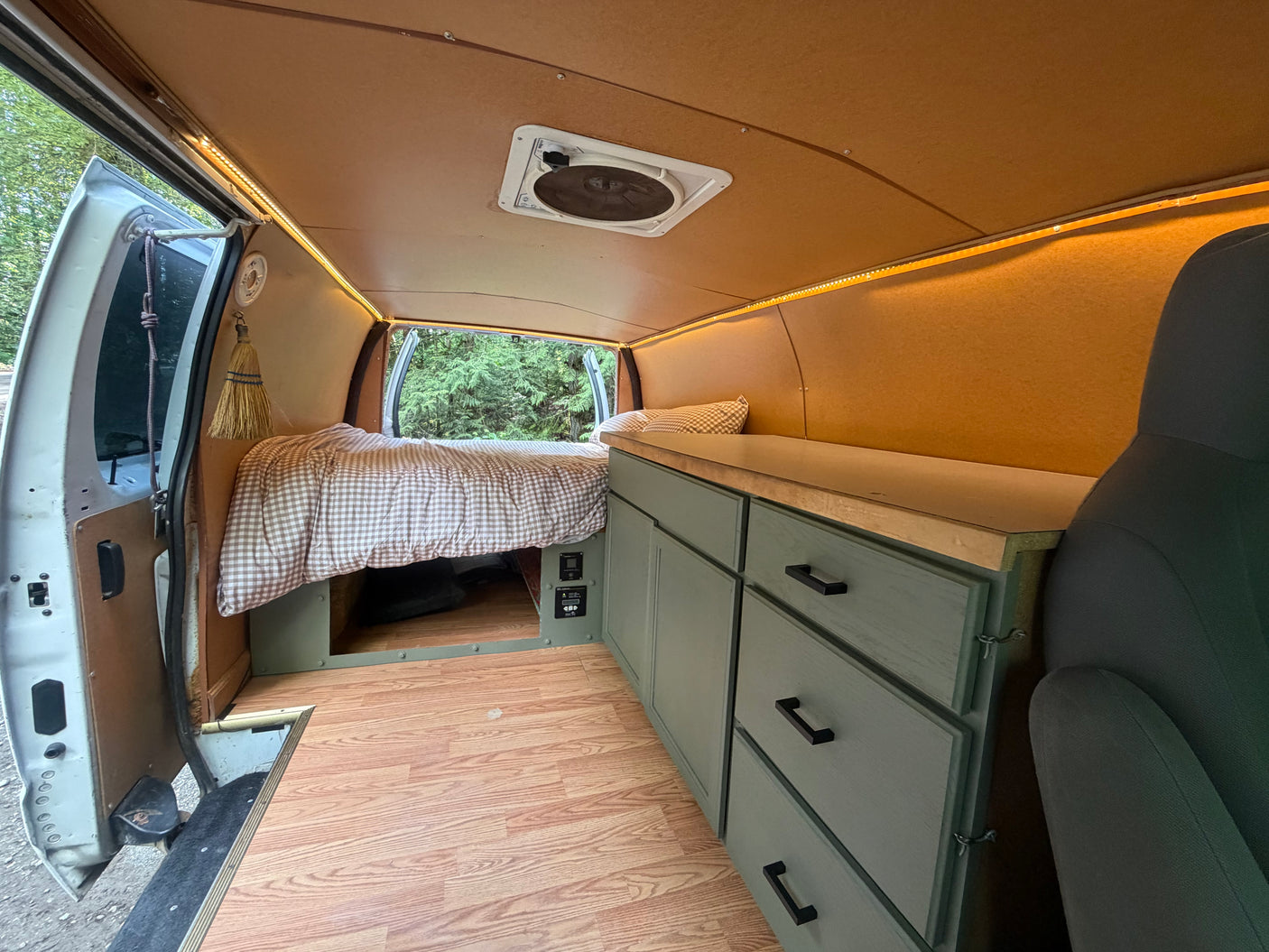 Explore nature in this RV rental! Custom van interior features a comfy bed, green cabinets, wood floor, and LED lights.