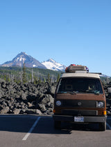 Brown RV rental van parked against a stunning backdrop of snowy mountains and volcanic rock.