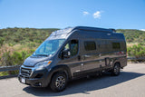 Modern gray Winnebago camper van, excellent for rv rental journeys, parked on asphalt beside green hills.