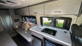 Inside an RV rental: Compact kitchen with sink & cooktop, overhead storage, and lounge seating. Ideal for travel.