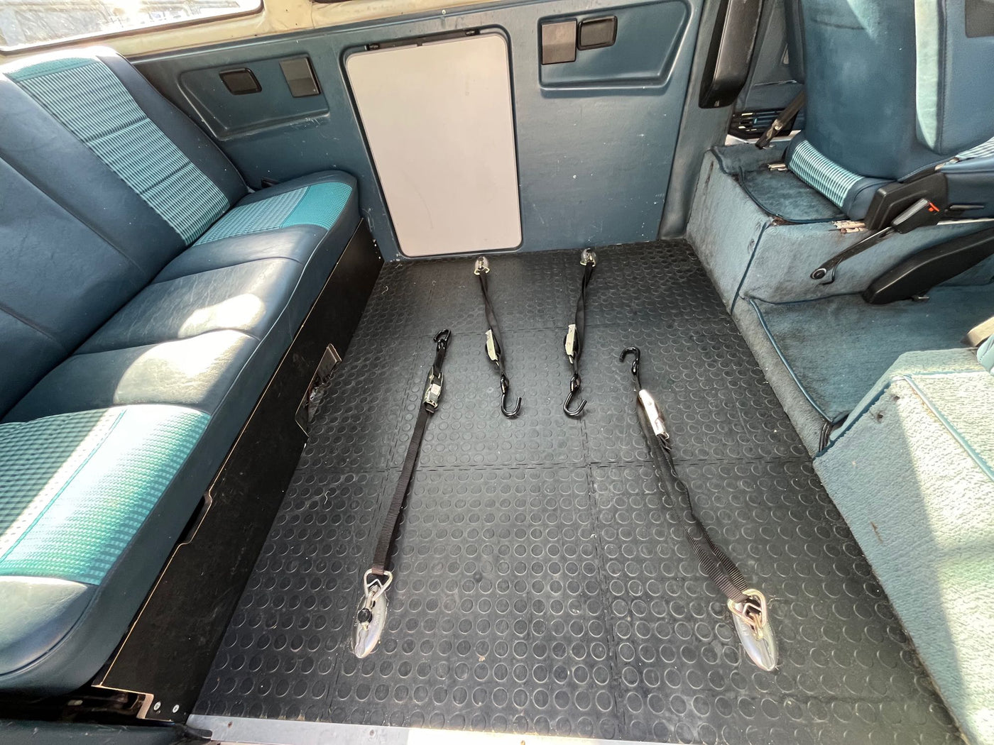Inside this RV rental van: a comfy blue/green patterned bed, practical rubber flooring, and large windows. — photo 8