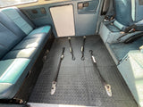 Inside this RV rental van: a comfy blue/green patterned bed, practical rubber flooring, and large windows.