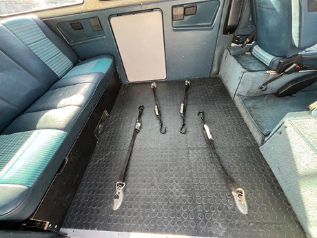 Inside this RV rental van: a comfy blue/green patterned bed, practical rubber flooring, and large windows.