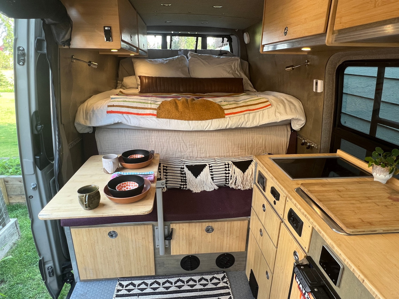 Cozy RV rental interior featuring a rear bed, compact kitchen, and a small dining table with settings. — photo 19
